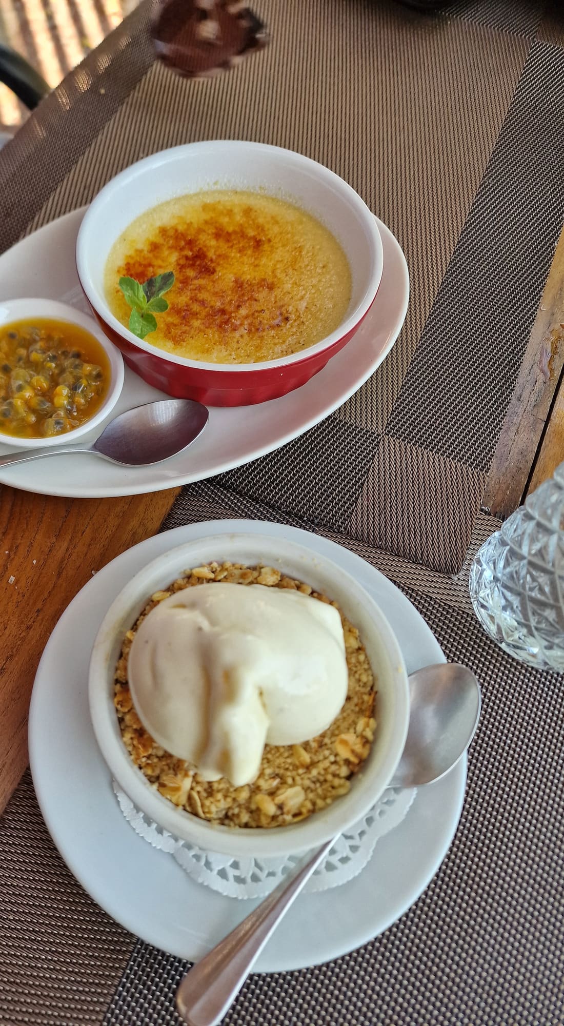 A creme brulee with a caramelised top beside a crumble topped with cream, on a wooden table.