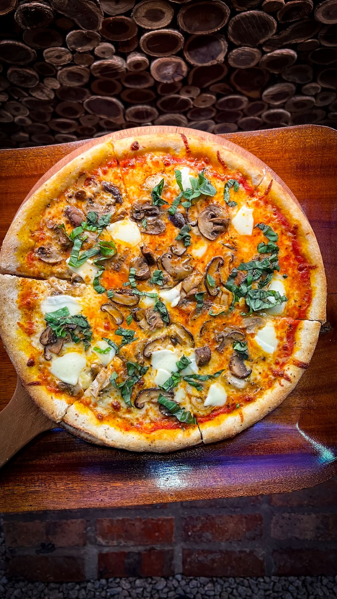 A mushroom pizza with melted cheese and fresh basil, served on a wooden board.