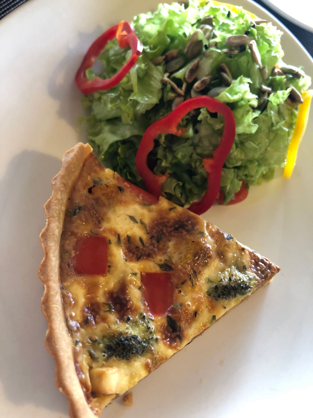 A wedge of broccoli and tomato quiche beside a green salad with seeds and red pepper rings.